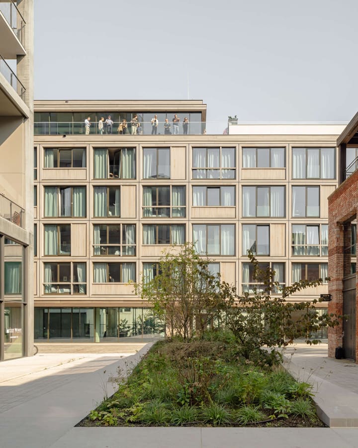 A green courtyard between the buildings with planters, paths and the timber hotel facade