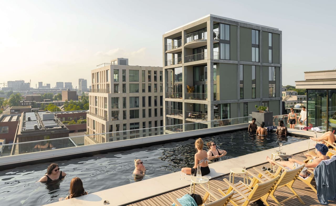 Photo, July 2024: residents swimming in the rooftop pool, with the green Superlofts tower and the white block behind